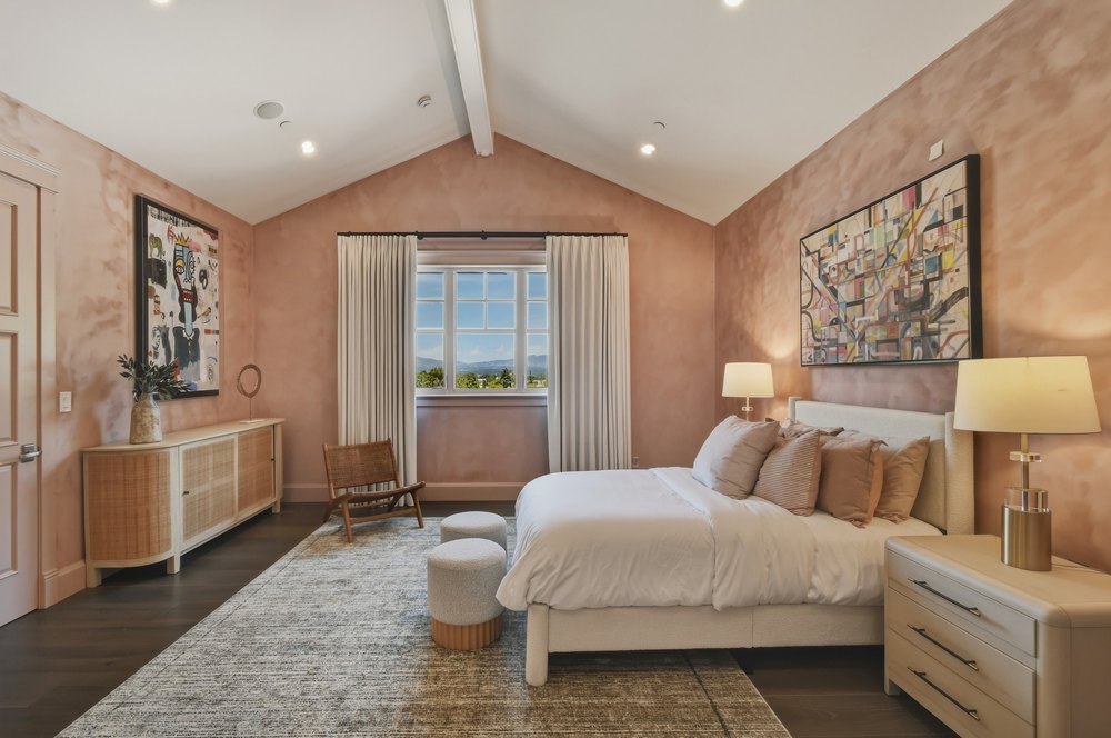 Vaulted Bedroom with Soft Pink Accent Walls, Upholstered Bed, and Large Windows