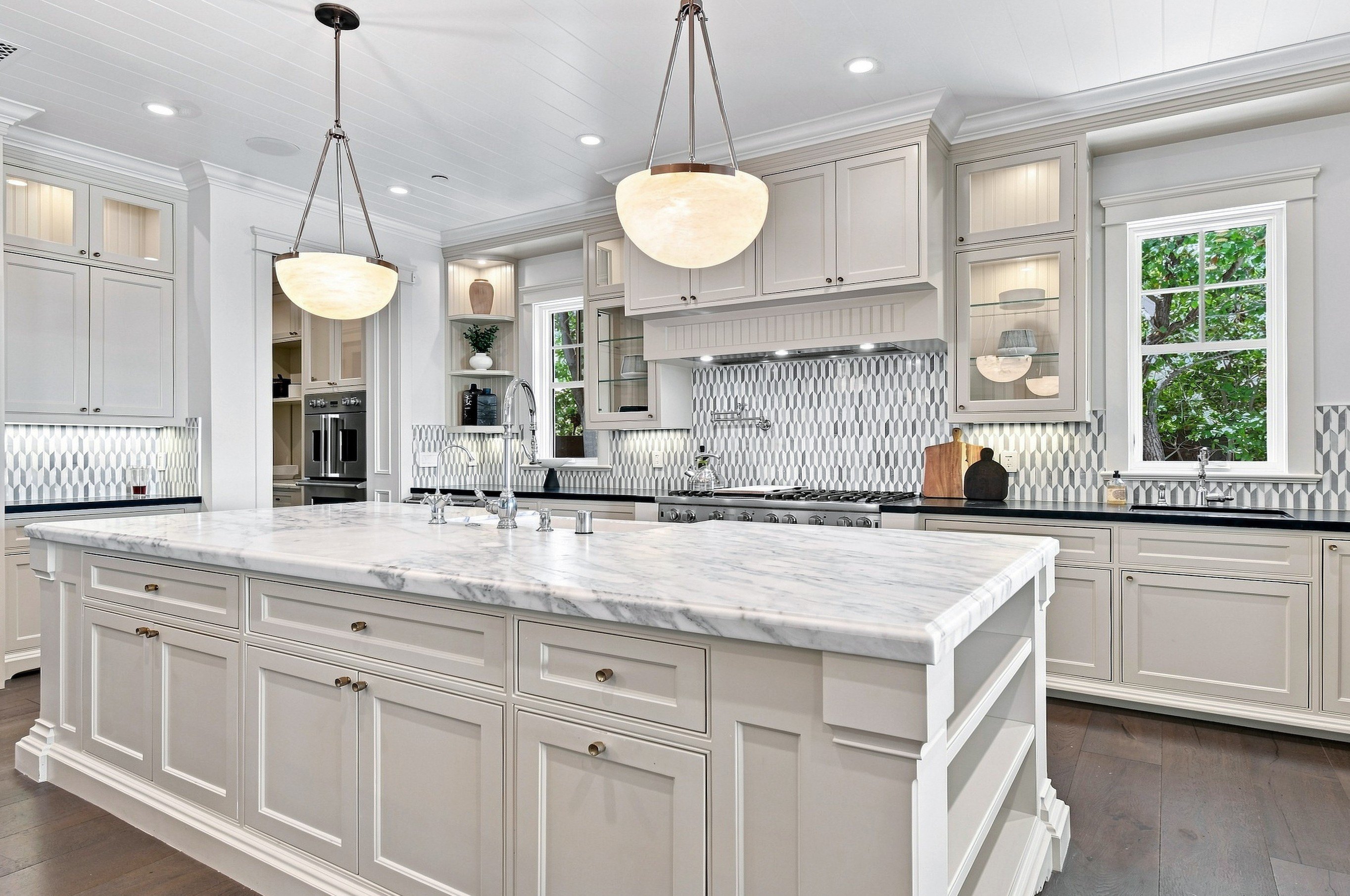 Spacious Kitchen with Large White Island, Marble Countertops, and Pendant Lighting