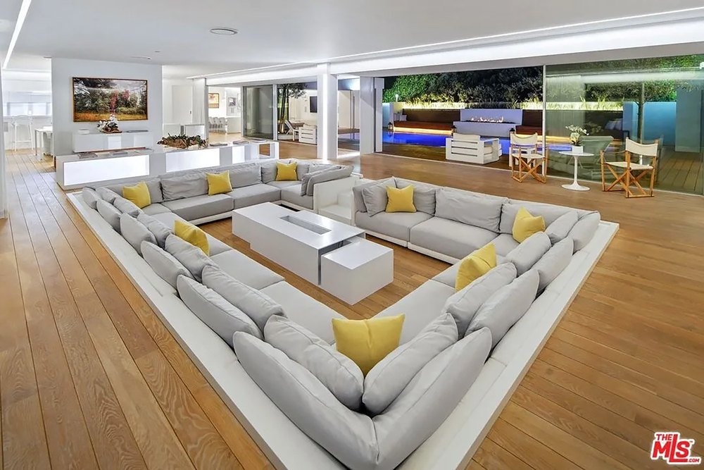 Spacious contemporary living room featuring a massive U-shaped sunken sofa and pool views.
