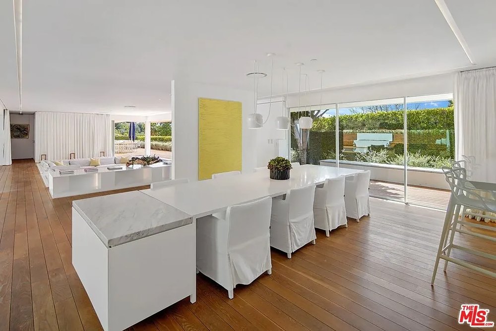 Minimalist open-plan dining room with a long white table and floor-to-ceiling windows.