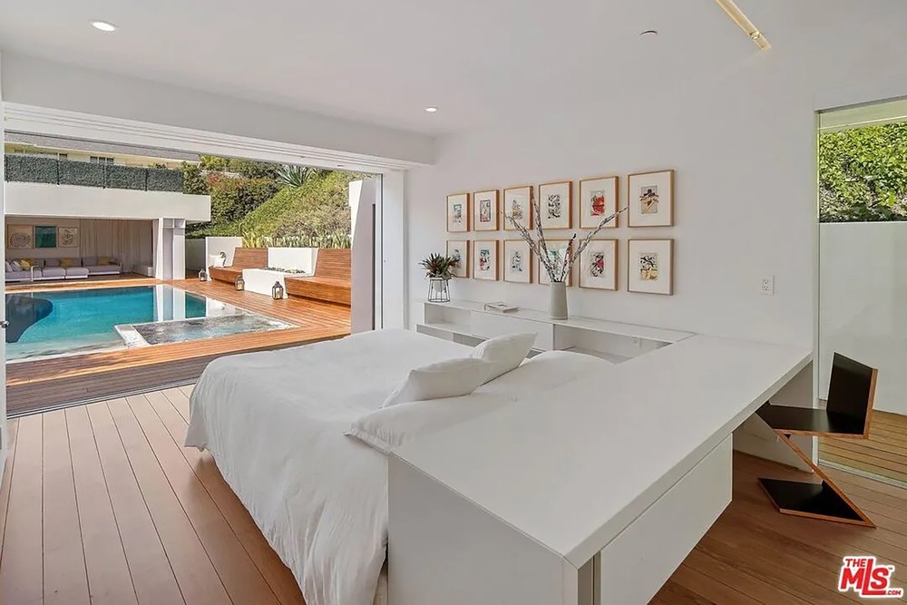 Minimalist master bedroom with a white platform bed, built-in desk, and direct pool access.