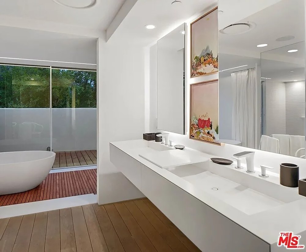 Modern primary bathroom featuring a floating double vanity, large mirrors, and a glimpse of an outdoor soaking tub.