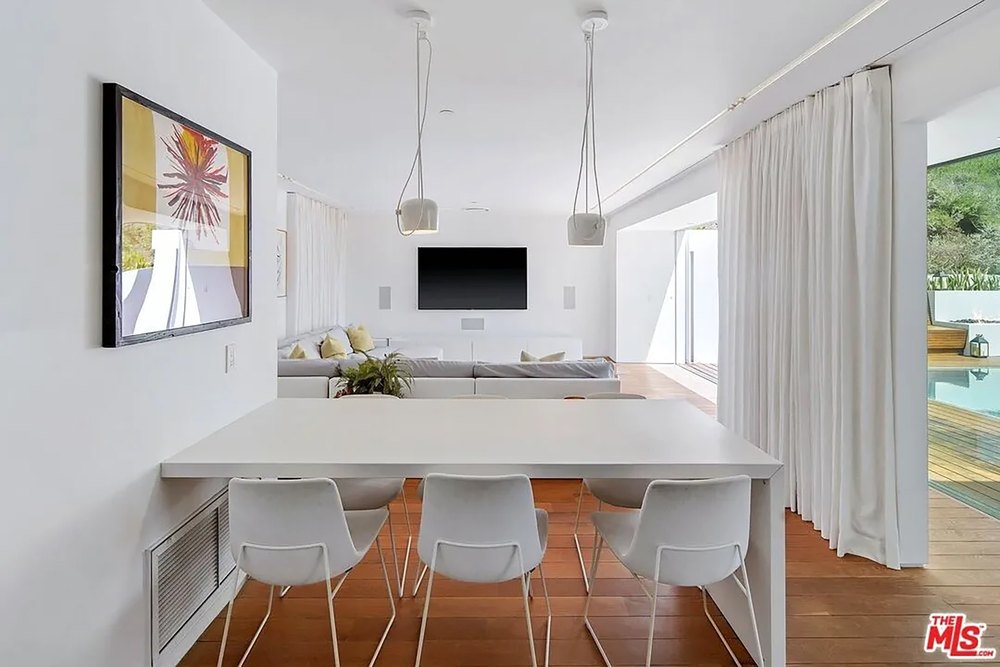 Bright open-concept living and dining area with minimalist white furniture and wood flooring.