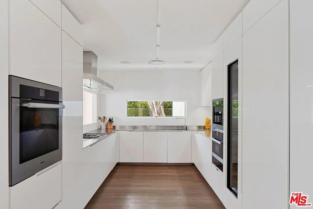 Sleek all-white minimalist kitchen with built-in appliances and a U-shaped countertop layout.