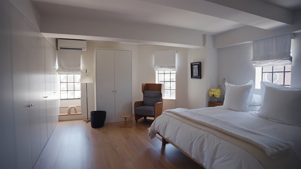Minimalist Primary Bedroom with White Bedding, Armchair, and Built-In Closets
